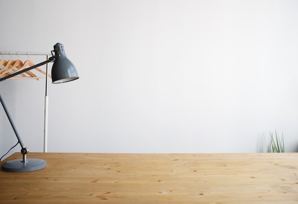 A clean wooden desk with a balanced-arm lamp, soft natural light